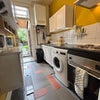 Photo 4: A view of the kitchen including oven, electrical cooker, washing machine and storage.